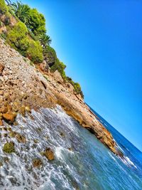 Rock formations by sea against clear blue sky