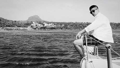 Portrait of young man sitting on sea against sky