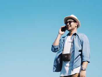 Low angle view of smiling man using phone against clear blue sky