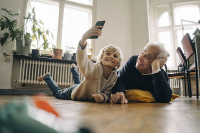 Grandfather and grandson lying on the floor at home taking a selfie