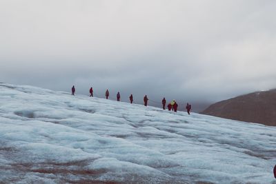 People walking on snow covered mountain against sky