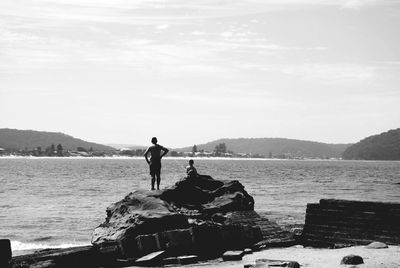 Man standing on rock by sea against sky