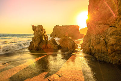 Rocks on sea shore against sky during sunset