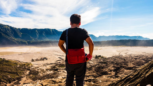 Rear view of man standing on mountain against sky