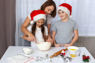 Mom and children in red caps cooking christmas cookies in the kitchen.