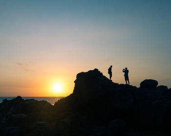 Silhouette people standing on rock against sky during sunset