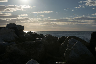 Rocks by sea against sky during sunset