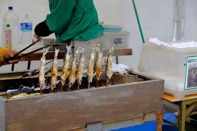 Vendor cooking fish on barbecue grill in market