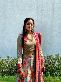 Portrait of smiling young woman standing against wall