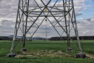 Wind turbines on grassy field against cloudy sky