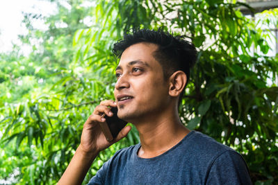 Portrait of young man looking away against trees