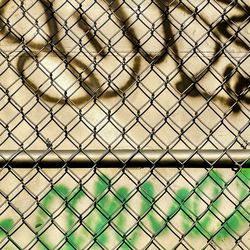 Full frame shot of chainlink fence with graffiti background 