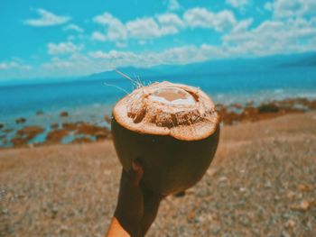 Close-up of hand holding ice cream cone at beach against sky