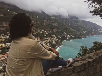 Woman sitting on retaining wall while looking at view