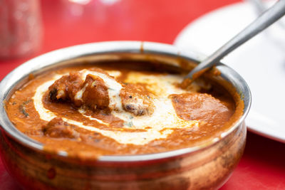 Close up view of a bowl of chicken butter masala - an indian food served on red table