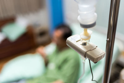 Close-up of iv drip with man on bed in hospital