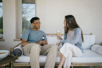 Young man and woman with drinks sitting on sofa in patio