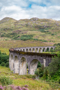 Bridge by mountain against cloudy sky