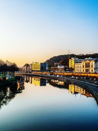 Bridge over river in city against clear sky during sunset