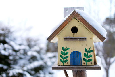 Close-up of birdhouse on snow covered field against sky