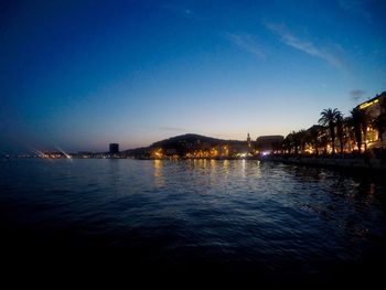 Illuminated city by sea against sky at night