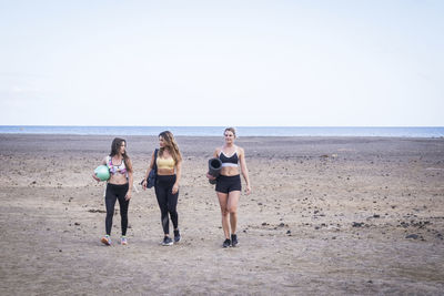 Full length of friends walking at beach against sky