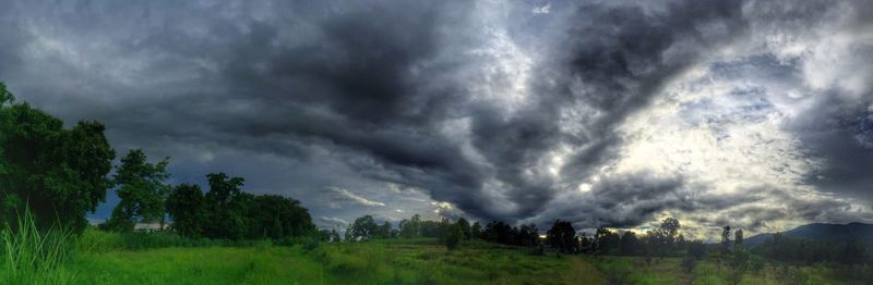 Silhouette of trees on landscape against cloudy sky