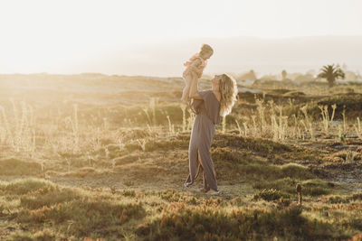 Mom and young toddler girl playing at beach during sunset