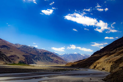 Scenic view of road by mountains against blue sky