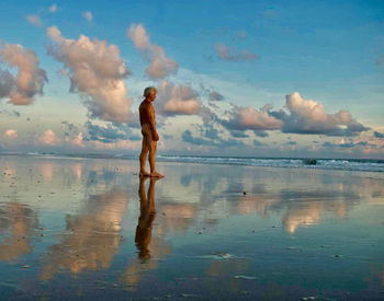 Full length of nude man standing on beach.