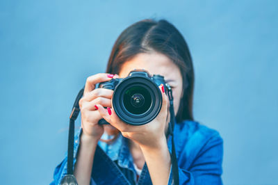 Woman photographing through camera against blue background