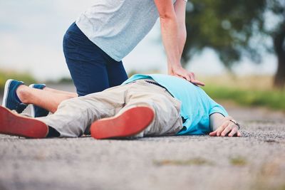 Low section of man resuscitating friend lying on road