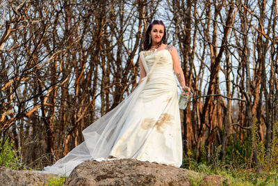 Portrait of young woman in dirty wedding dress standing in forest