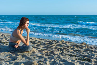 Woman sitting on shore at beach against sky