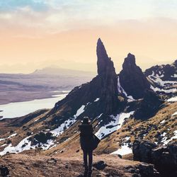 Rear view of man standing on mountain during winter at sunset