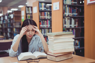 Woman suffering headache while reading book on table in library