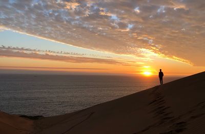 Silhouette person standing on beach against sky during sunset