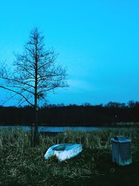 Bare trees on calm lake against clear blue sky