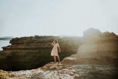 Woman standing on rock looking at sea against clear sky