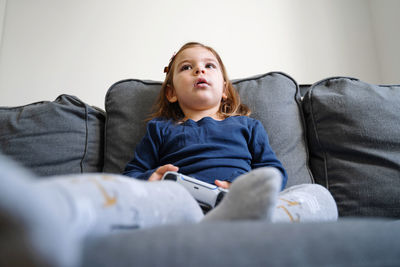 Girl looking away while sitting on sofa at home