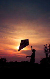 Silhouette man holding umbrella on field against sky during sunset