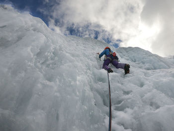 Woman climbing on frozen mountain against sky