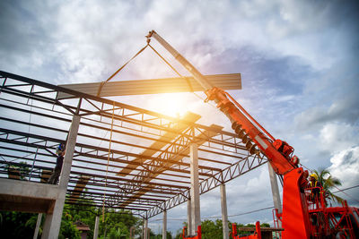 Asian crane drivers are steering cranes to install metal sheet, industrial roof installation.