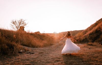 Rear view of bride dancing on field against clear sky