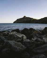 Rocks by sea against clear sky