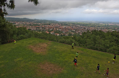 People on field by cityscape against sky