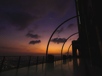 Silhouette fence by sea against sky during sunset