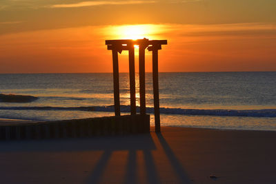 Silhouette wooden posts on beach against sky during sunset