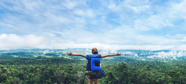 Rear view of woman jumping on mountain against sky