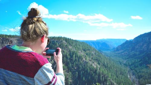 Rear view of woman photographing mountains against sky at oak creek canyon
